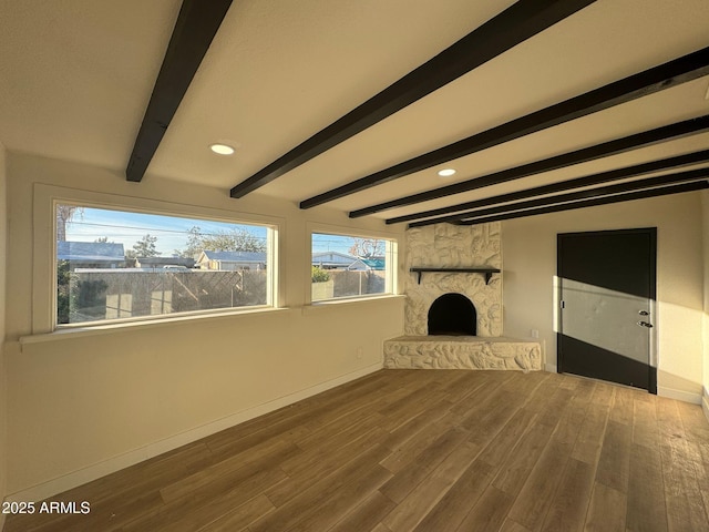 unfurnished living room with a stone fireplace, hardwood / wood-style floors, and beam ceiling