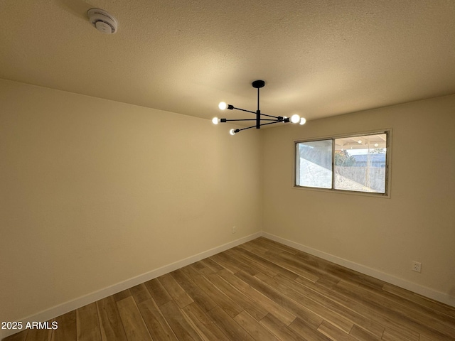 unfurnished room featuring hardwood / wood-style floors, a notable chandelier, and a textured ceiling