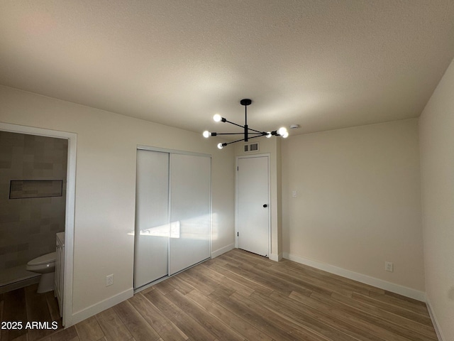 unfurnished bedroom featuring an inviting chandelier, wood-type flooring, a closet, and a textured ceiling