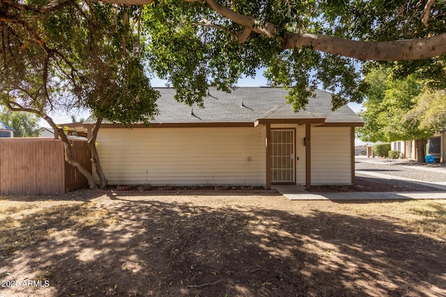 single story home featuring a shingled roof and fence