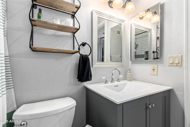 bathroom featuring toilet, a textured wall, visible vents, and vanity