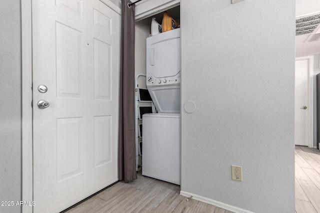 laundry area with light wood-style flooring, laundry area, stacked washer and dryer, visible vents, and baseboards