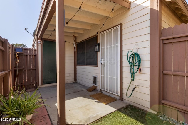 view of exterior entry with fence and a patio