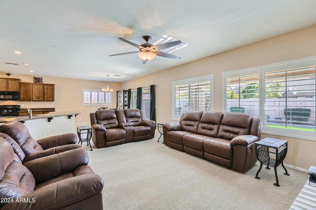 carpeted living room with ceiling fan with notable chandelier