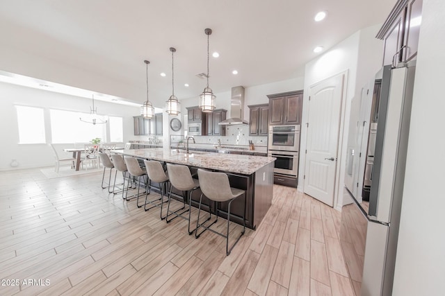 kitchen with a large island, stainless steel appliances, pendant lighting, wall chimney exhaust hood, and sink