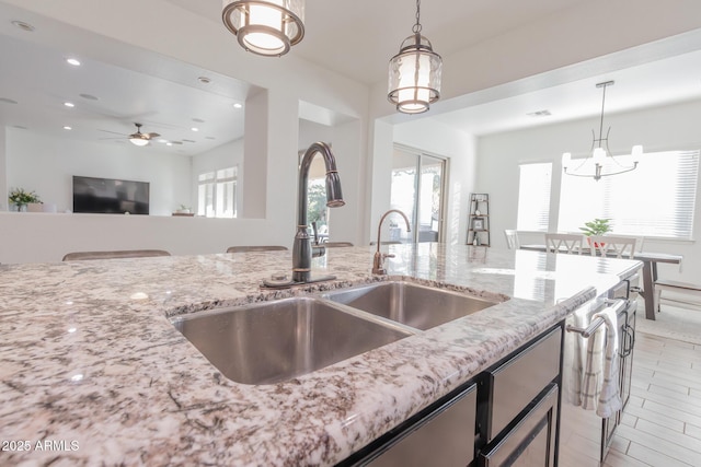 kitchen with ceiling fan with notable chandelier, light stone countertops, pendant lighting, and sink