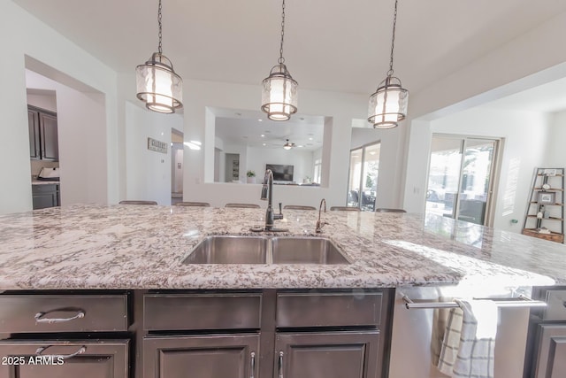 kitchen with light stone countertops, hanging light fixtures, ceiling fan, dark brown cabinets, and sink