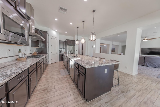 kitchen with hanging light fixtures, a spacious island, appliances with stainless steel finishes, ceiling fan, and dark brown cabinets