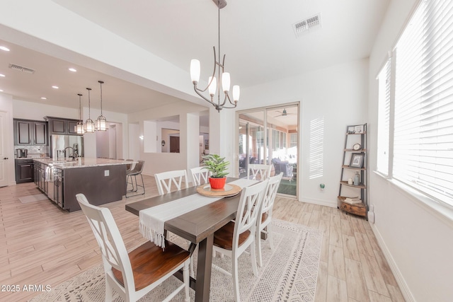 dining room with sink, light wood-type flooring, and ceiling fan with notable chandelier