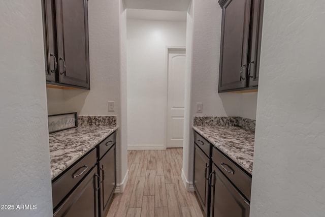 kitchen with dark brown cabinets, light hardwood / wood-style flooring, and light stone countertops