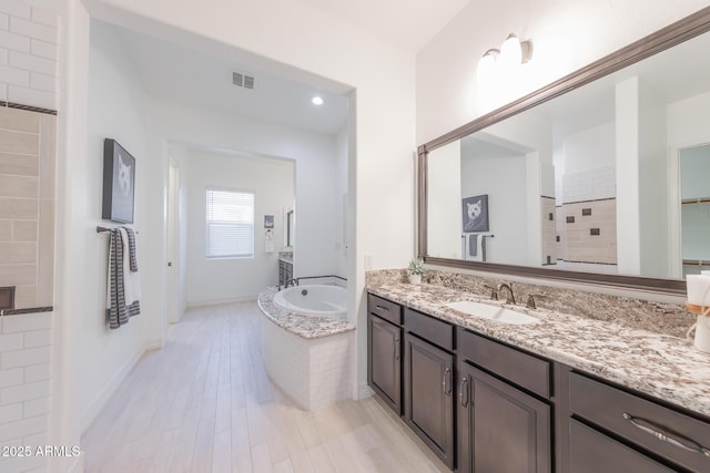 bathroom featuring vanity, tiled tub, and hardwood / wood-style flooring