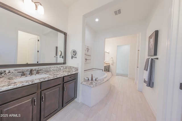 bathroom with hardwood / wood-style floors, vanity, and a relaxing tiled tub