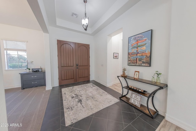 tiled entrance foyer featuring an inviting chandelier and a raised ceiling