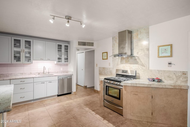 kitchen with sink, wall chimney range hood, tasteful backsplash, light tile patterned floors, and appliances with stainless steel finishes