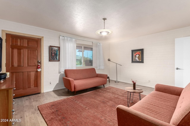 living room with brick wall, a textured ceiling, and light wood-type flooring