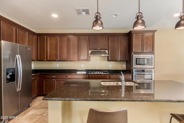 kitchen featuring visible vents, dark stone counters, under cabinet range hood, a sink, and appliances with stainless steel finishes