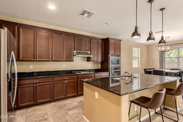 kitchen with visible vents, a breakfast bar area, under cabinet range hood, a sink, and stainless steel appliances