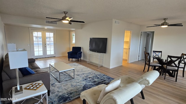 living room featuring ceiling fan, french doors, hardwood / wood-style floors, and a textured ceiling