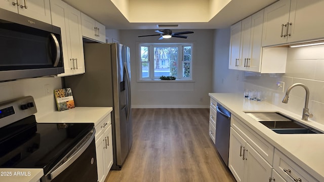 kitchen featuring appliances with stainless steel finishes, white cabinetry, sink, light wood-type flooring, and ceiling fan