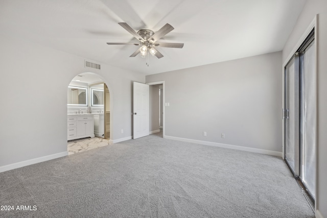 unfurnished bedroom with multiple windows, ceiling fan, ensuite bathroom, and light carpet