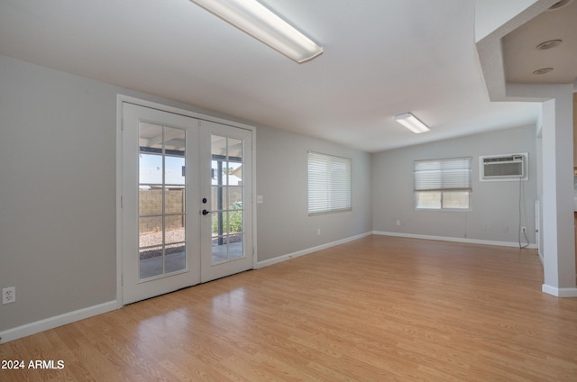 empty room with a wealth of natural light, light wood-type flooring, a wall unit AC, and french doors