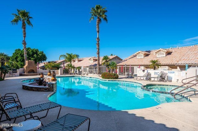 view of swimming pool featuring a patio area, a community hot tub, and exterior fireplace