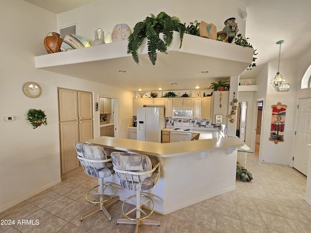 kitchen with a breakfast bar area, light brown cabinetry, pendant lighting, and white appliances