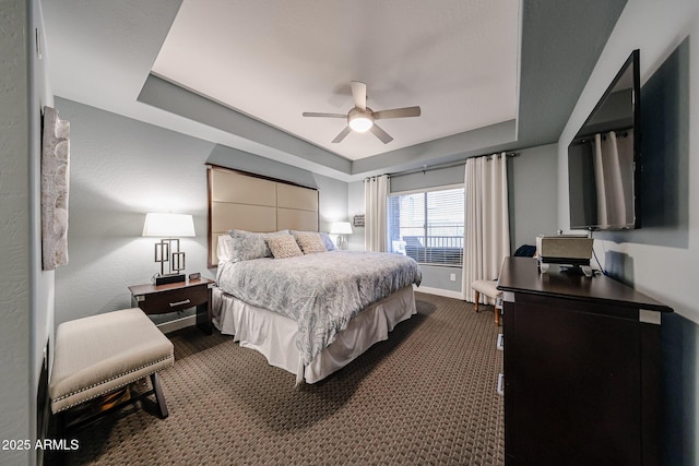 bedroom with dark carpet, a ceiling fan, a raised ceiling, and baseboards