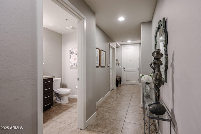 corridor with light tile patterned floors, recessed lighting, baseboards, and a textured wall