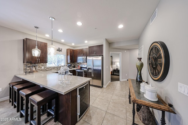 kitchen featuring stainless steel appliances, wine cooler, dark brown cabinetry, a peninsula, and light countertops