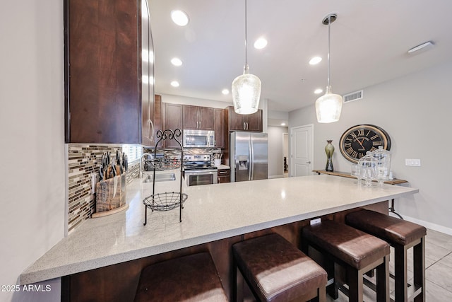 kitchen featuring tasteful backsplash, dark brown cabinets, a peninsula, stainless steel appliances, and a sink
