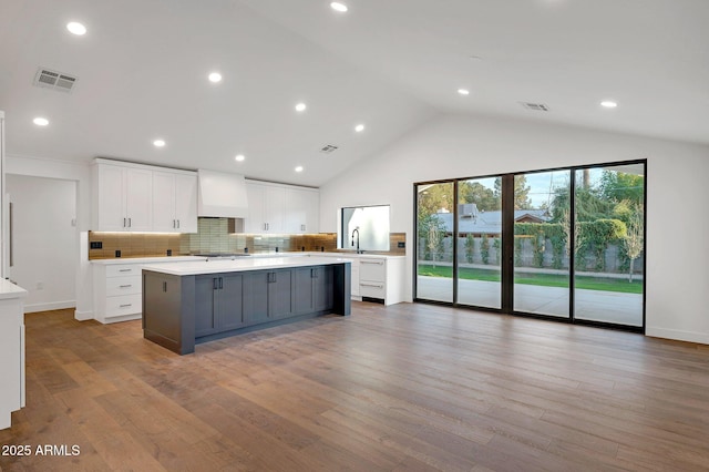 kitchen with premium range hood, visible vents, white cabinets, light countertops, and light wood-type flooring