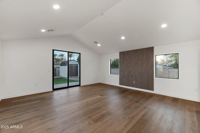 empty room with vaulted ceiling, wood finished floors, visible vents, and baseboards