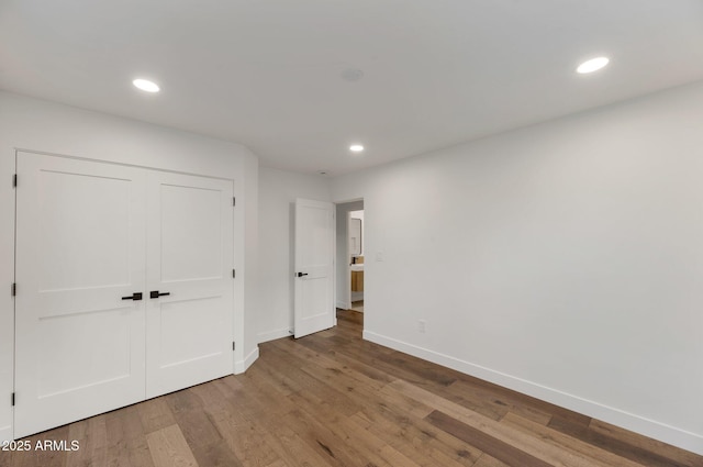 unfurnished bedroom featuring a closet, recessed lighting, wood finished floors, and baseboards