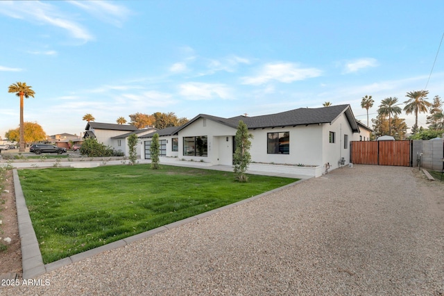 view of front facade featuring driveway, stucco siding, a gate, and a front yard