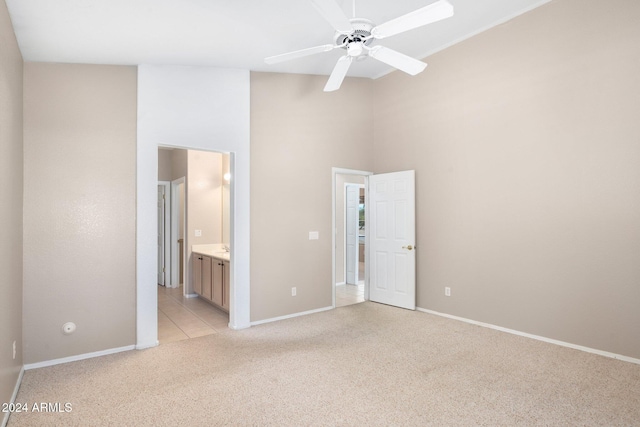 unfurnished bedroom featuring connected bathroom, a high ceiling, light carpet, and ceiling fan