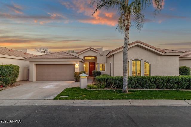 mediterranean / spanish-style home featuring a yard, stucco siding, an attached garage, driveway, and a tiled roof