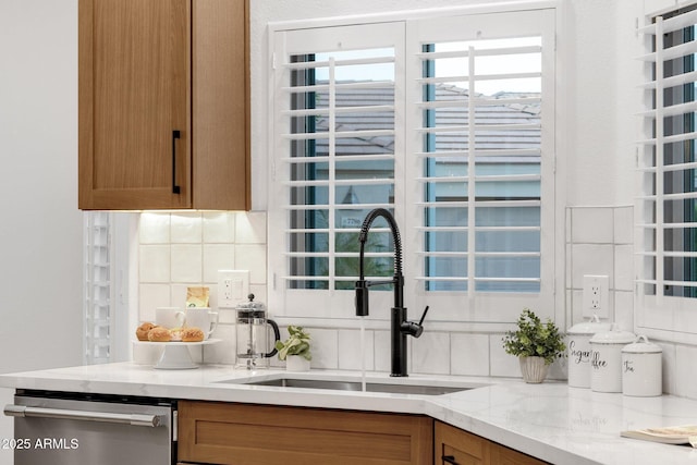 kitchen with brown cabinets, tasteful backsplash, a sink, light stone countertops, and dishwasher