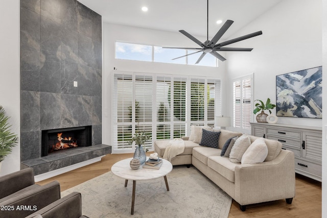 living area with a ceiling fan, a high ceiling, light wood-style floors, a fireplace, and recessed lighting