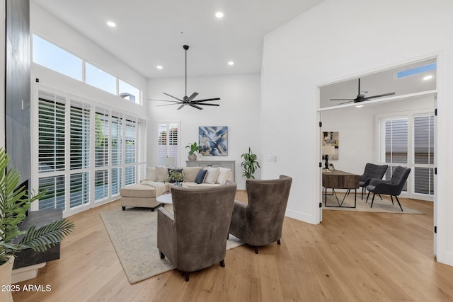 living room with light wood-style floors, recessed lighting, ceiling fan, and a high ceiling