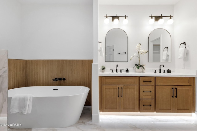 bathroom featuring double vanity, marble finish floor, a freestanding bath, and a sink