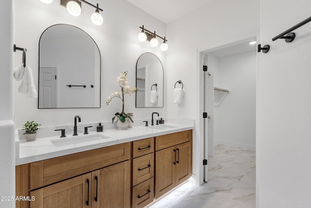 full bath with double vanity, marble finish floor, a walk in closet, and a sink