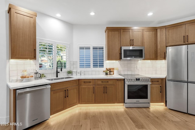 kitchen with stainless steel appliances, a sink, light countertops, light wood-type flooring, and tasteful backsplash