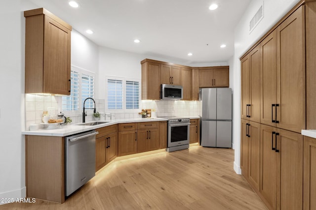 kitchen with stainless steel appliances, a sink, visible vents, light wood-type flooring, and decorative backsplash