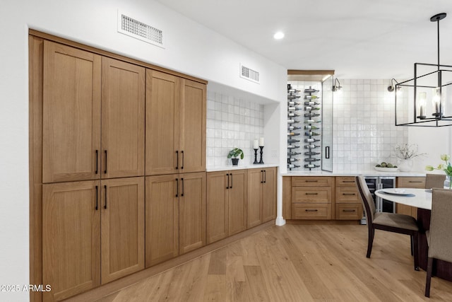 kitchen with wine cooler, visible vents, light countertops, light wood finished floors, and tasteful backsplash