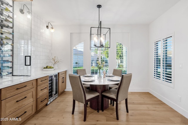 dining room with beverage cooler, an inviting chandelier, light wood-style flooring, and baseboards