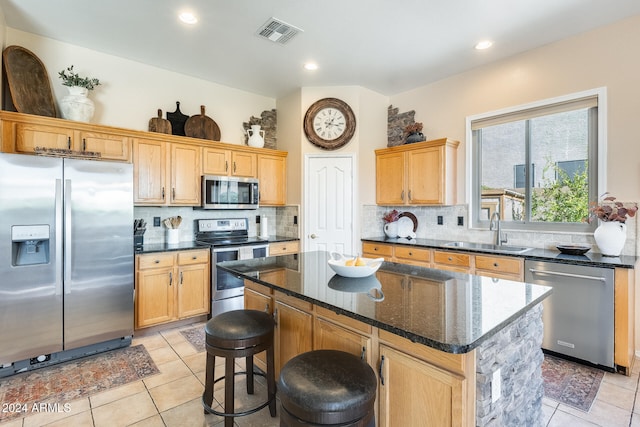 kitchen with stainless steel appliances, dark stone counters, light tile patterned floors, sink, and a center island