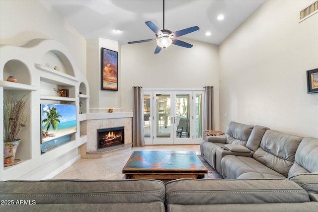 tiled living room with built in shelves, french doors, high vaulted ceiling, a tile fireplace, and ceiling fan