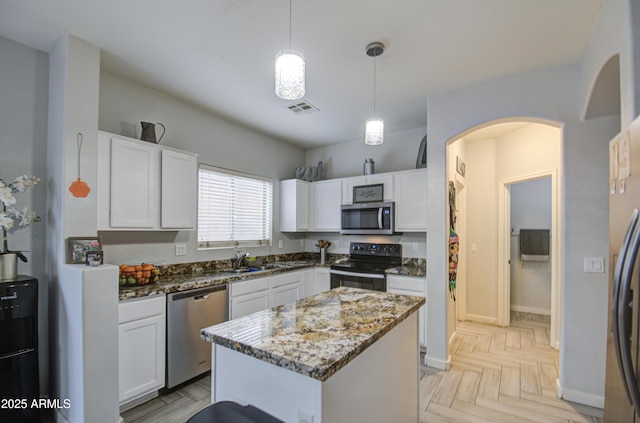 kitchen with a kitchen island, appliances with stainless steel finishes, decorative light fixtures, white cabinetry, and dark stone countertops