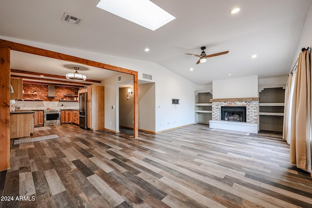 unfurnished living room featuring ceiling fan, vaulted ceiling with skylight, built in features, and light wood-type flooring